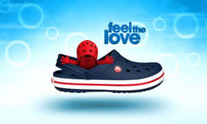 紅色卡通角色從藍色 Croc 鞋中彈出，帶有 'feel the love' 標語。 — Crocs 壁紙