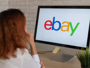 穿白襯衫的人在桌前思考，顯示器上有eBay標誌。 — eBay 壁紙