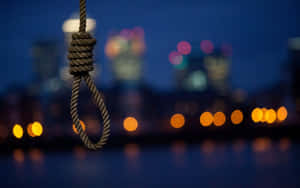 一個絞索懸掛在夜間城市景觀中，帶有模糊燈光。 — 自殺 壁紙