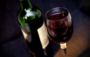 深色木桌上的綠色酒瓶和一杯紅酒。 — 葡萄酒 壁紙