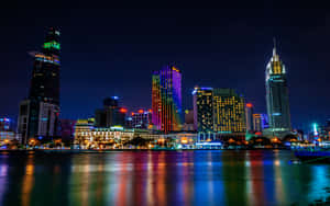夜間城市天際線，色彩繽紛的燈光倒映在水面上。 — MacBook Pro 16 壁紙