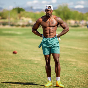 有刺青的運動型男人站在草地上，穿著青綠色短褲和黃色鞋子。 — Dk Metcalf 壁紙
