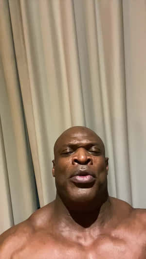 一個赤裸上身的肌肉發達光頭男人閉著眼睛，在室內靠近米色窗簾站立。 — 運動 壁紙
