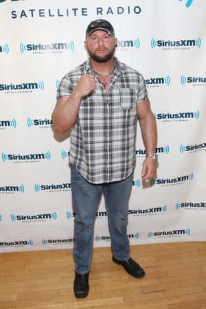 男人穿著格紋襯衫和牛仔褲在SiriusXM活動中舉起拳頭擺姿勢。 — 運動 壁紙