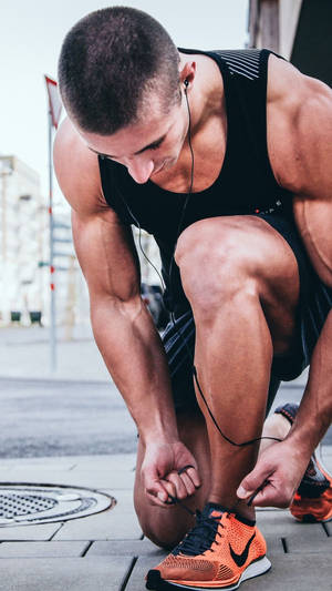 運動型男人在城市人行道上繫著他的橙色跑鞋。
