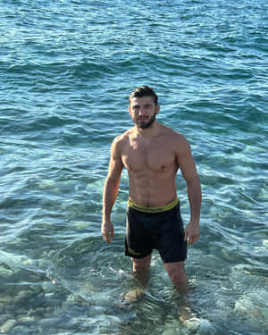 一個健美的男人站在淺海水中，下方岩石可見。 — 海洋 壁紙