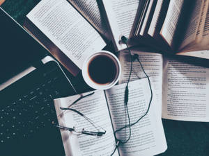 打開的書本、眼鏡和咖啡杯放在筆記型電腦鍵盤上以供閱讀。