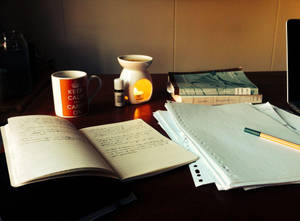 舒適的學習書桌，有打開的筆記本、杯子和溫暖發光的擴散器。 — 讀書 壁紙