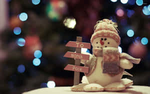 雪人公仔舉著指向北極的標誌，背景有模糊的聖誕燈飾。 — 可愛聖誕節 壁紙