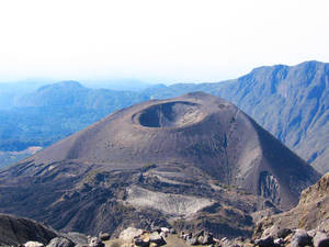 朦朧天空下，遠處有層層山峰的山上的火山口。 — 坦尚尼亞 壁紙