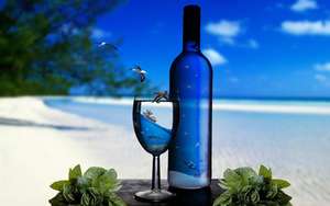 藍色酒瓶和酒杯，裡面有海洋場景，放在沙灘桌上，有綠葉。 — 海灘 壁紙