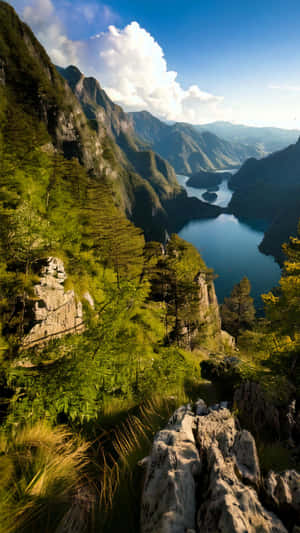 在藍天白雲下，一個藍綠色湖泊被陡峭的綠色山脈和岩石峭壁環繞的風景如畫的景色。 — 山脈 壁紙