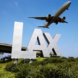 陽光明媚的日子裡，LAX機場標誌上有飛機飛過。 — 加州 壁紙