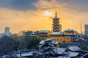 夕陽下被雪覆蓋的金色寶塔寺廟，背後有現代城市天際線。 — 唐人街 壁紙