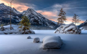 暮色中冰雪覆蓋的岩石和山脈的冰凍湖泊 — 冬季風景 壁紙