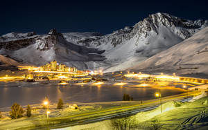 被雪覆蓋的山村在夜晚亮起燈光，燈光反射在結冰的湖面上。 — 酷寒冬季 壁紙