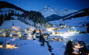 被雪覆蓋的山村，黃昏時分有發光的窗戶和教堂。 — 冬季風景 壁紙