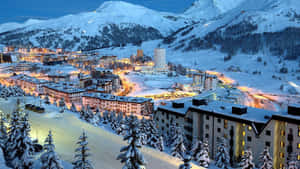 被雪覆蓋的山村在黃昏時被照亮，有松樹和建築物。 — 暮光 壁紙