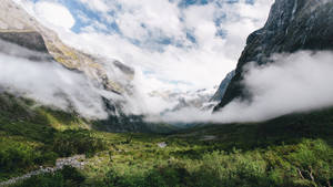 迷霧山谷被高聳的綠色山脈環繞，天空多雲。 — 丘陵景觀 壁紙