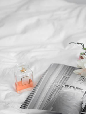 一個香水瓶和 Chanel 雜誌放在白色床上，伴有一朵蘭花。 — 香奈兒 壁紙