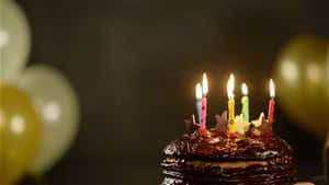 巧克力生日蛋糕，配上點燃的蠟燭和背景中的氣球。 — 生日快樂蛋糕 壁紙