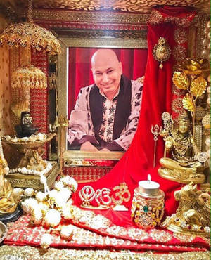 一個裝飾華麗的宗教神殿，有金色雕像、紅布和一個微笑男子的裱框肖像。 — 金廟 壁紙