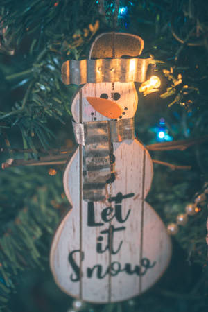 木製雪人裝飾品，帶有「Let it Snow」文字，掛在點亮的聖誕樹上。 — 白雪公主 壁紙