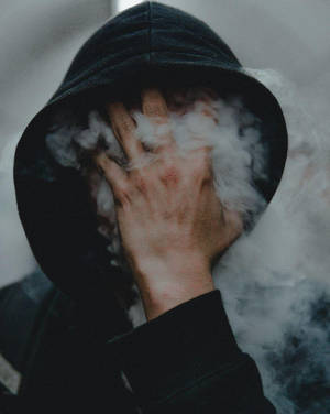 身穿深色連帽衫的人用手遮住臉，白色蒸氣在周圍翻騰。 — 抽菸 壁紙