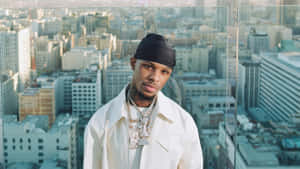 身穿白色外套和黑色頭巾的男人在城市天際線窗前擺姿勢。 — Toosii 壁紙