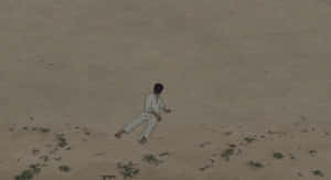 一個穿白衣的人獨自坐在荒蕪的景觀中，散落著綠色斑塊。 — 酷炫烏龜 壁紙