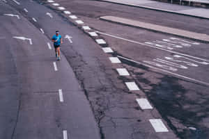 一個人在有白色方向箭頭的裂縫城市道路上跑步。 — Running 壁紙