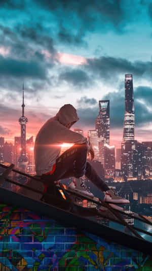身穿連帽上衣的人坐在塗鴉牆上，俯瞰黃昏時燈火通明的城市。 — 獨自一人 壁紙