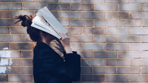 人用打開的書遮臉，靠磚牆 — 讀書 壁紙