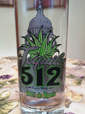 Tequila 512 Blanco 瓶子，帶有龍舌蘭和國會大廈設計，放在花卉桌布上。 — 3:4 壁紙