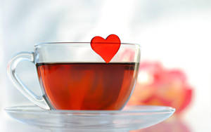 一個玻璃茶杯，裡面有紅茶和一個心形標籤，放在碟子上。 — 可愛桌面 壁紙