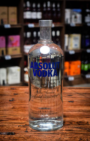 透明Absolut Vodka瓶子在木吧檯上，後面有酒架。 — Galaxy Tab 壁紙