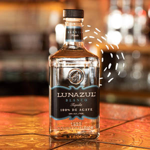 木吧檯上的一個Lunazul Blanco龍舌蘭酒瓶，背景燈光模糊。 — 品牌 壁紙