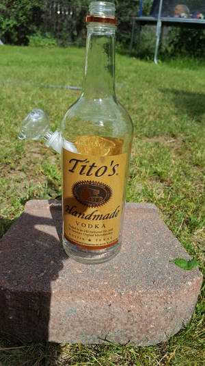 Tito's伏特加酒瓶與水煙槍配件，放在草地上的磚上。 — 品牌 壁紙