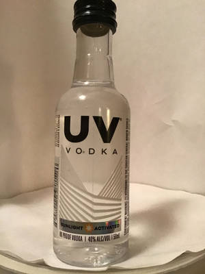 一個小小的透明伏特加酒瓶，黑色瓶蓋和幾何標籤，在白色紙巾上。 — 高清 壁紙