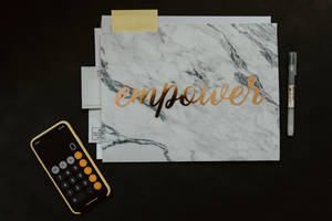 大理石文件夾帶金色箔片 'empower' 文字，旁邊有計算機和筆在黑色桌上。 — 會計 壁紙