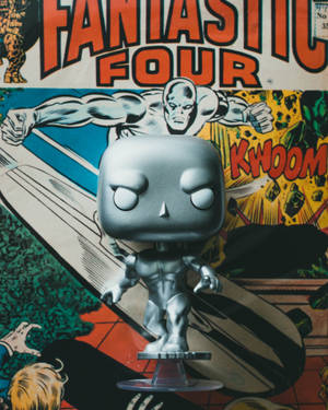 銀色衝浪手Funko Pop！人偶放在透明支架上，背景是驚奇四超人漫畫封面。 — Funko Pop 壁紙