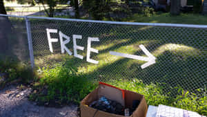 鐵絲網圍欄上畫有「FREE」，指向一個裝有廢棄物品的紙箱。 — 免費 壁紙