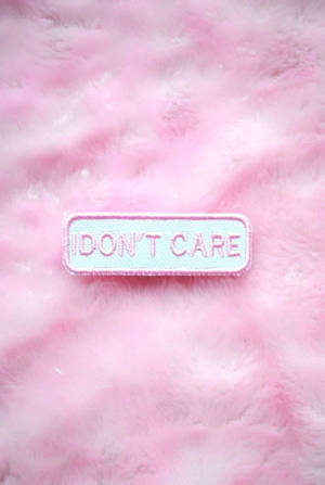 一個寫著 'I DON'T CARE' 的補丁在毛茸茸的粉紅色布料上。 — 我不在乎 壁紙