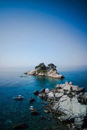 小岩石島嶼上有松樹，周圍是清澈的藍色海水和船隻。 — 法羅群島 壁紙