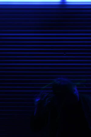 夜晚，藍色霓虹燈照亮的金屬百葉窗前一個人的剪影。 — 美學藍色 iPhone 壁紙