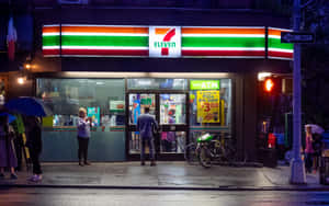 撐著雨傘的人們在雨夜站在7-Eleven商店外。 — 7-ELEVEN 壁紙