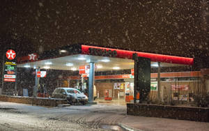 雪花飄落在亮燈的加油站，一輛車停在簷篷下。 — 加油站 壁紙