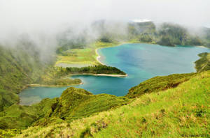 一個在霧氣瀰漫的火山口中，被綠色山丘環繞的寧靜綠松石色湖泊。