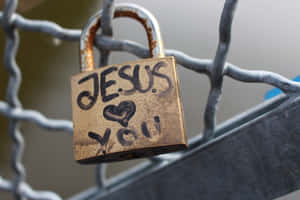 一個青銅掛鎖，上面寫著「JESUS ❤️ YOU」，掛在鐵絲網圍欄上。 — 耶穌基督 壁紙