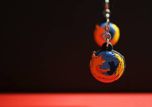 Firefox標誌鑰匙圈懸掛，背景模糊，表面紅色。 — 高清 壁紙